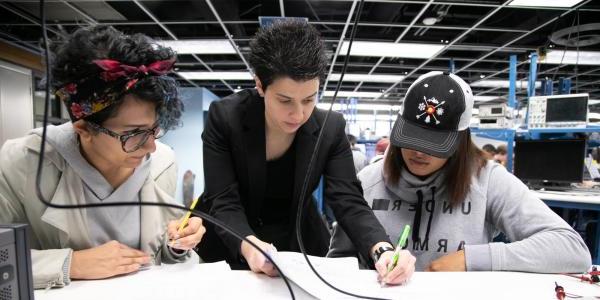 A faculty member helps two students with an assignment during a lab session